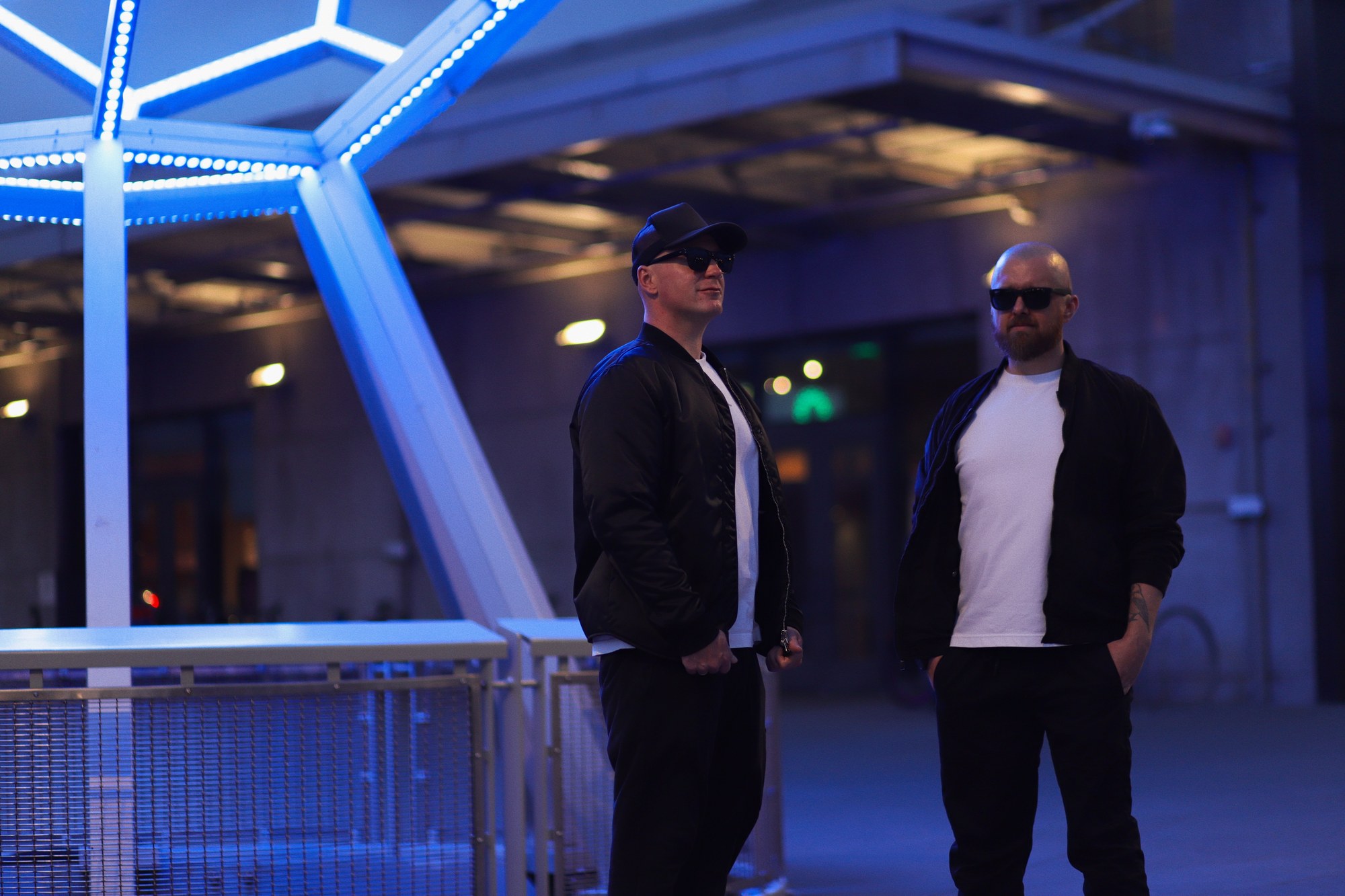 Mission Control founders Anton Zykin and Dima Tsozik beside a blue-lit geometric sculpture at dusk