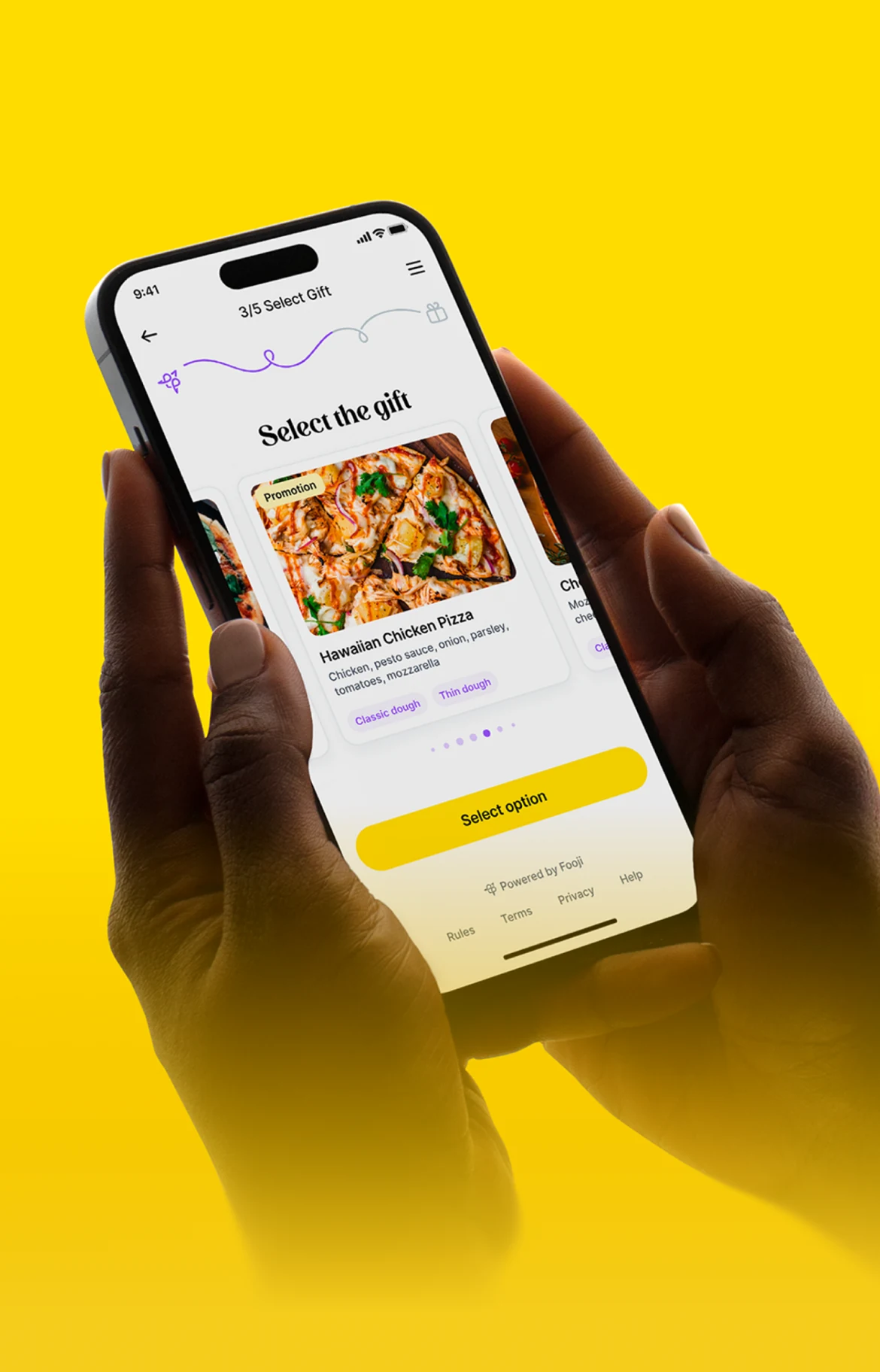 Hands holding a phone with Fooji’s gift-selection experience against a yellow background